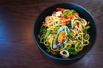 Spicy Spaghetti with Seafood in black dish on wooden table, Top view