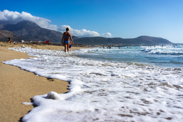 Woman walk along the beach, leaving a trail in the sand.