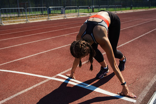 Female teen athlete in sportswear with smartwatch on her wrist preparing for run in starting position