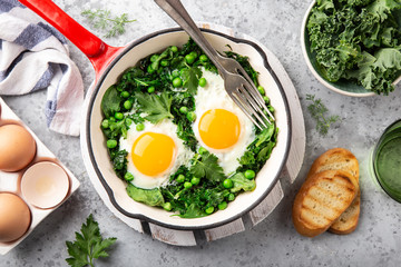 Healthy breakfast. fried eggs with kale, spinach and green peas in red skillet