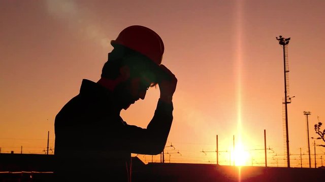 Sagoma di un ingegnere edile e civile mentre indossa il caschetto di sicurezza visto di profilo. Scena al rallentatore al tramonto.