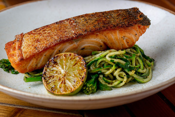 Home made dish of salmon with pice of roasted lemon and a side of green noddles