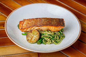 Home made dish of salmon with pice of roasted lemon and a side of green noddles