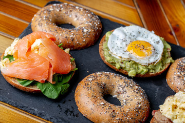 Bagels Selection with cream cheese smoked salmon, eggs and avocados bacon and salmon on rustic wooden background