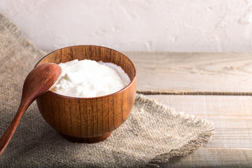 Wooden bowl with homemade yogurt on  wooden table near white wall. 