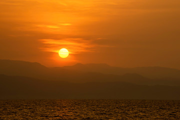 Golden light of sunrise behind the mountains and the sea.