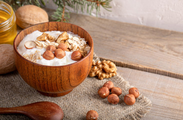 Wooden bowl with yogurt with rolled oats and nuts on burlap napkin on wooden planks.