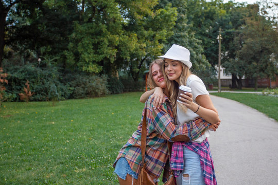 Two young girls hung each other in the park and one of her holding coffee to go on hand