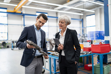Businessman and senior businesswoman examining workpiece in a factory