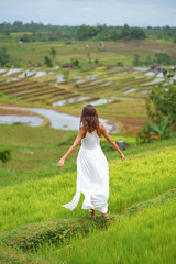 Fototapeta na wymiar A young woman with her arms outstretched posing standing on a hill. In the background are rice fields