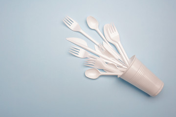 Single-use plastic products: plastic cutlery, cups on bright blue background