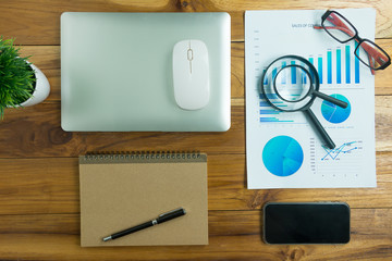 Top view of a wooden desk color with a computer graph, magnifier and office business calculator.
