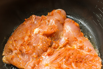 Raw chicken breast fillet marinated in hot spices cooked roasted in slow cooker.
