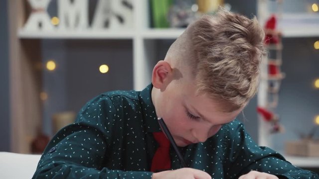 Serious boy concentrated on painting with color pencils on white paper at the brown wooden table. Select focus on face, shallow depth. Education concept, art class, enjoying the art process