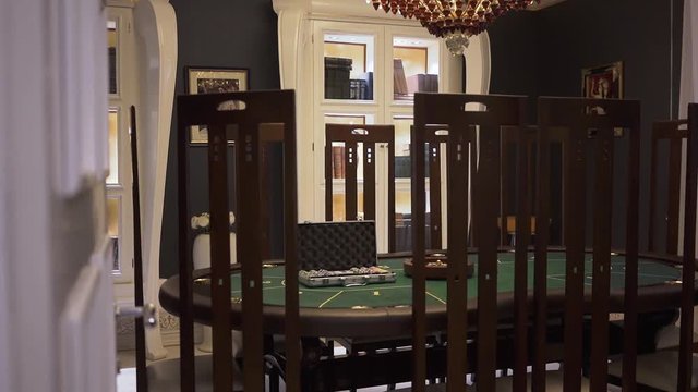 The gaming table with green surface with poker set on it in modern casino, high back chairs standing near. Comfortable place with luxary interior waiting for the guests