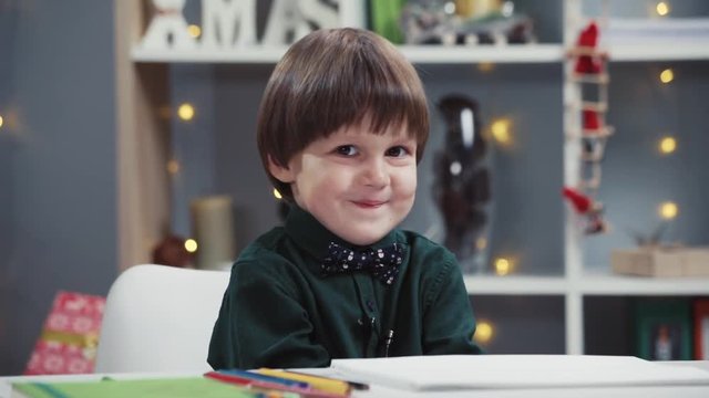 Close Up View Of Little Shy Boy With A Bowtie Cutely Smiling. Indoors Shooting, Art Class, Lights On The Background. Happy Childhood, Having Fun, Early Childhood Education Concept. Child�s Portrait