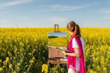 girl painter with an easel in a yellow rapeseed field