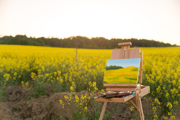 easel with paints and canvas painting in the field