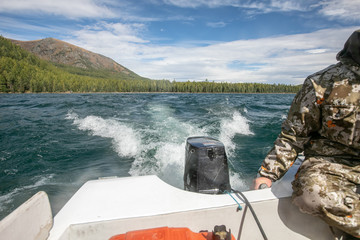 The man in a camouflage on the lake. view of the mountains and the river from a motor boat