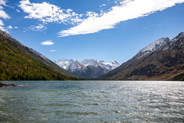 landscape with mountains, green trees and blue lake on a  cloudy sky background