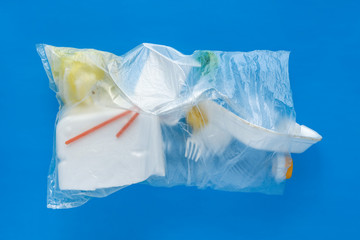 plastic waste straw bottle fork container in transparent bag on blue background
