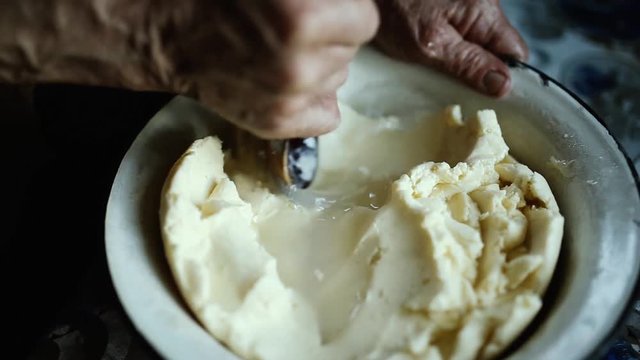hands of an old woman with a wooden spoon, whip homemade butter with whey