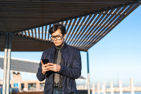 Portrait of fashionable young businessman wearing glasses and tie looking at mobile phone