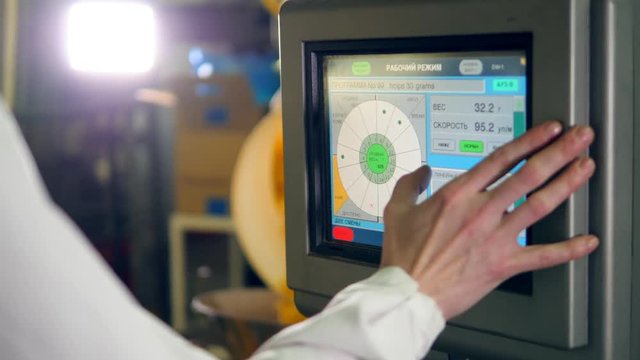 A person uses a machine to control work of a conveyor with potato crisps at a factory.