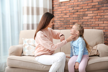 Young woman checking little girl's pulse with fingers at home