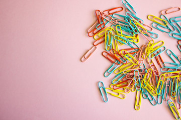 Pink background with colored stationery for paper scattered on it. paper clips on a pink background, office theme. Colorful Back to School background. Top view, flat lay.