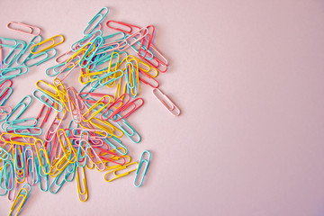 Pink background with colored stationery for paper scattered on it. paper clips on a pink background, office theme. Colorful Back to School background. Top view, flat lay.