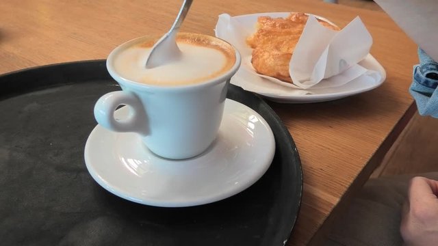 spoon mixing cappuccino on the wooden table of a cafe bar. People having italian breakfast with sugar pastry on background.