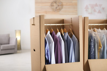 Cardboard wardrobe boxes with clothes on hangers in living room