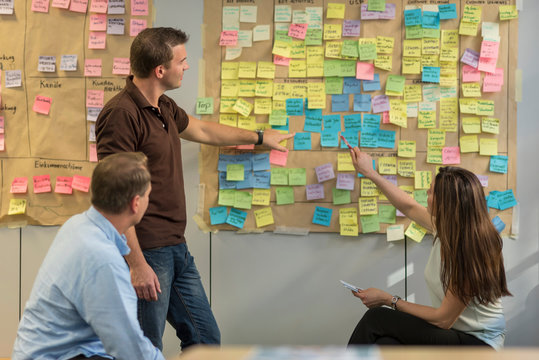 Colleagues discussing with sticky notes at wall in office