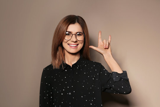 Woman showing I LOVE YOU gesture in sign language on color background