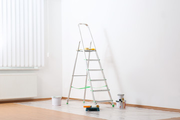 Stepladder and painting tools near wall in empty room