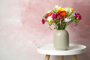 Bouquet of spring freesia flowers in vase on table against color background, space for text