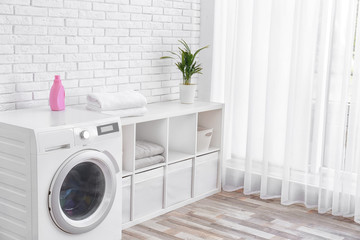 Modern washing machine near brick wall in laundry room interior, space for text