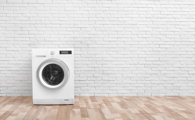 Modern washing machine near brick wall in empty laundry room, space for text - obrazy, fototapety, plakaty