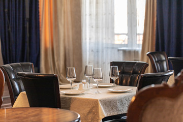 Banquet hall in the restaurant. Concept: Serving. Celebration. Anniversary. Wedding. White tablecloth, leather chairs, transparent glasses