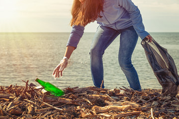 Woman cleans garbage on the beach, picks up the bottle. Ecology, earth day, cleaning of the...