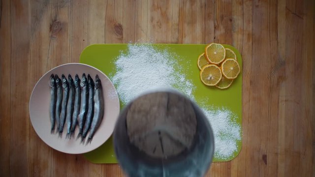 Top view of a man's hands covering a capelin with flour on a wooden table, the process of making a small silver fish, preparation for frying in oil in a pan.