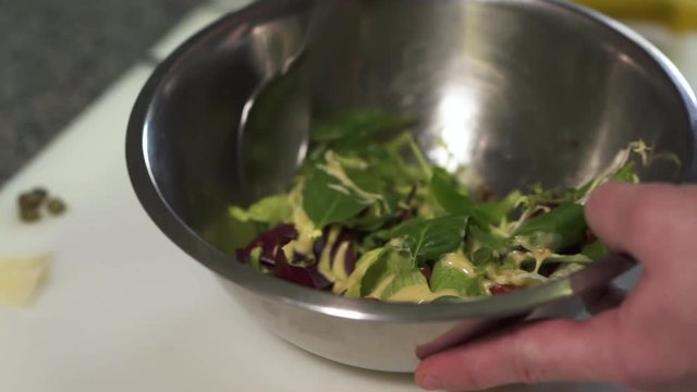 Chef hands holding big aluminium bowl with salad poured with sauce. The man mixing tometoes, spinach, arugula, lettuce and basil leaves close up. Cook preparing food in the kitchen. Healthy lifestyle
