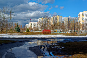 Urban houses and sky with clouds reflected in puddle from melting snow on street in day