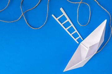 White paper boat with a white ladder and a piece of rope on a blue background