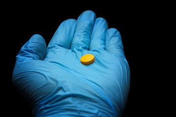 big yellow pill on the palm in a blue medical glove on a black background. hand in latex glove...