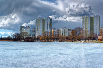 Fototapeta premium Urban houses and sky with clouds reflected in puddle from melting snow on street in day