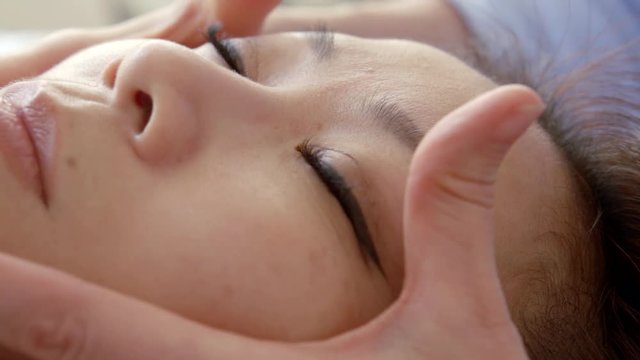 Face massage an Asian woman, along the lines of the cheekbones, eyebrows, hair, closeup portrait.