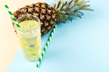 Pineapple and juice with ice in a glass, on a blue yellow background. Summer mood, copy space.