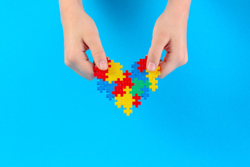 Child hand holding colorful heart on blue background. World autism awareness day concept